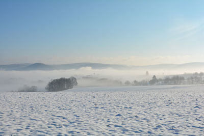 Snow landscape with fields and fog in the valley and with blue sky in spessart, bavaria, germany