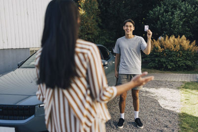 Happy young man showing drivers license to mother standing in back yard