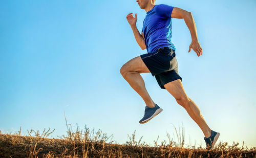 Low angle view of man jumping on field against clear sky