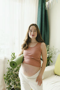 Smiling pregnant woman with exercise mat in living room