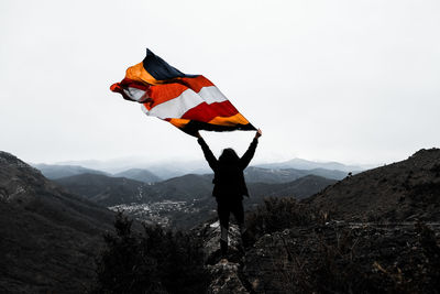 Woman with flag standing on mountain against clear sky