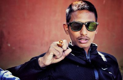 Young man with smoking pipe wearing sunglasses against wall