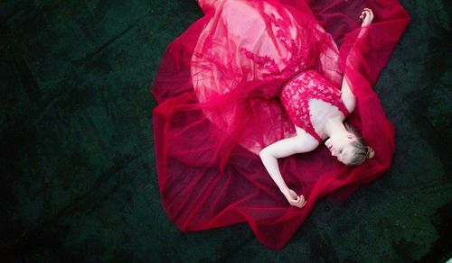 High angle view of young woman in red dress lying on floor