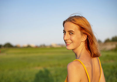 Portrait of young woman standing on field against sky