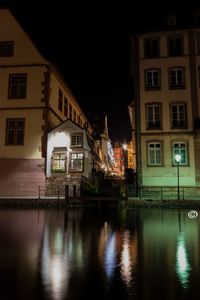 Illuminated buildings by river against sky at night