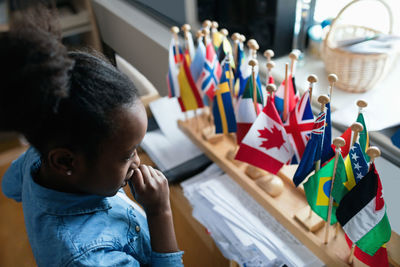 High angle view of thoughtful girl looking at various flags in classroom