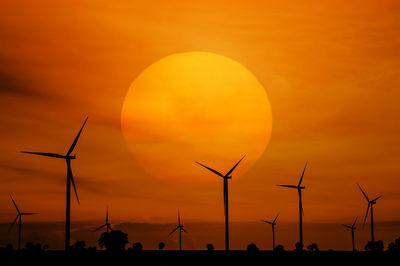 Silhouette of wind turbines against orange sky