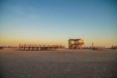 Pier on beach against clear sky during sunset