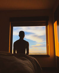 Rear view of shirtless man looking at window