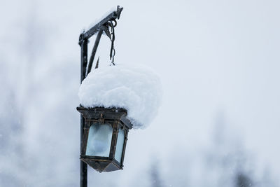An iron lantern hangs on a pole with a huge cap of snow.