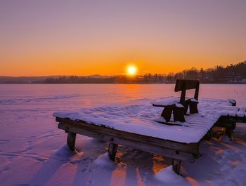 Scenic view of snow covered bench by lake during sunset