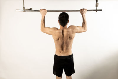 Rear view of shirtless man with arms raised against white background