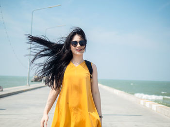 Young woman wearing sunglasses standing at beach against sky