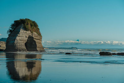 Rock formation in sea against clear blue sky