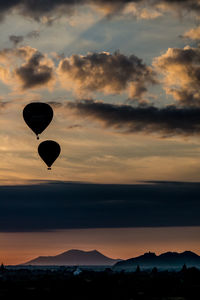 Silhouette hot air balloons flying over river against sky during sunrise
