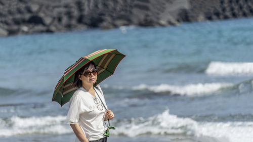 Young woman with umbrella standing at beach