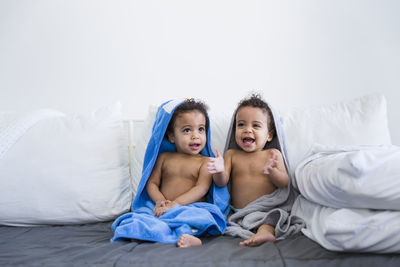 Cute sisters sitting side by side against wall on sofa