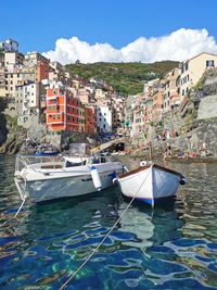 Sailboats moored on sea by buildings in city against sky