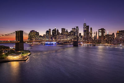 Illuminated bridge over river against buildings in city at night