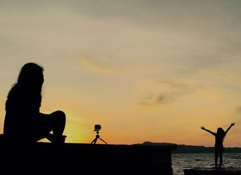 Silhouette people photographing sea against sky during sunset