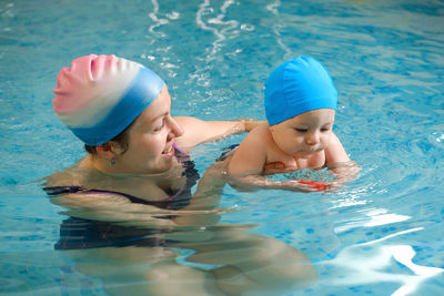 Early age swimming in pool. baby boy trained to swim in water coach woman in indoor swimming pool 