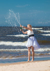 Woman splashing champagne at beach against clear sky