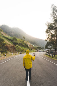 Rear view of man showing peace sign while standing on road