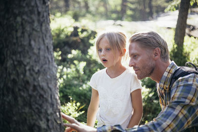 Father and daughter looking at tree trunk in forest