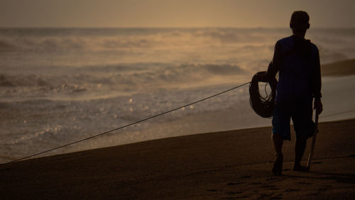 Rear view of man standing at beach during sunset