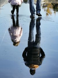Low section of man and daughter walking with reflection in puddle