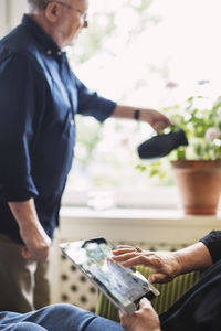 Cropped image of senior woman using digital tablet while man watering flower plant