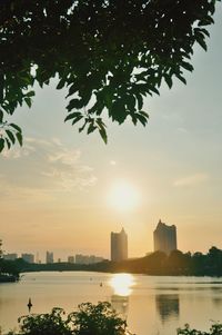 Scenic view of river by buildings against sky at sunset