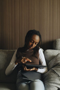 Girl using tablet pc while sitting on sofa at home