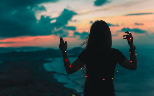 Rear view of woman photographing sea against sky during sunset