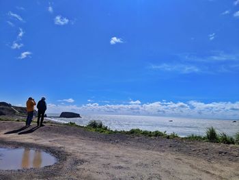 Friends standing at beach against blue sky