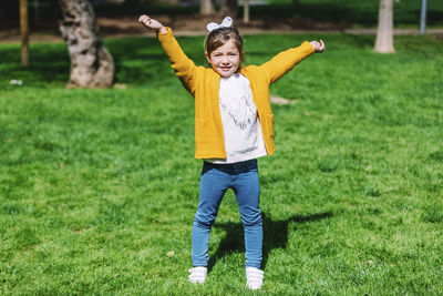 Portrait of cute smiling girl with arms outstretched standing on grassy field in park