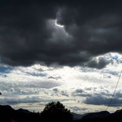 Low angle view of storm clouds over silhouette trees