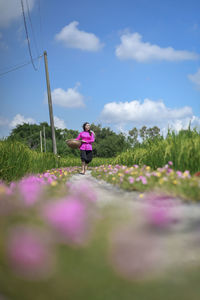 Woman with pink flowers on field against sky