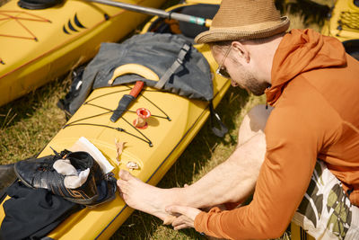 High angle view of man sitting on kayak and putting plaster on his foot
