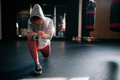 Strong unrecognizable female athlete in hoodie performing lunges exercise while training in modern gym with boxing equipment