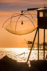 Scenic view of sea and fishing hut against sky during sunset