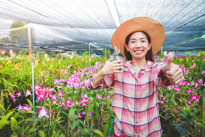 Portrait of smiling woman standing by flowering plants