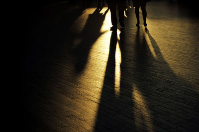 Low section of people walking on footpath during sunset