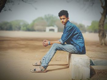 Portrait of young man sitting on retaining wall