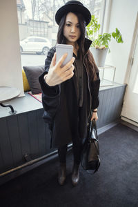 Full length of young businesswoman taking selfie while standing in modern office