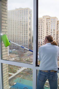 Rear view of woman standing by window in city