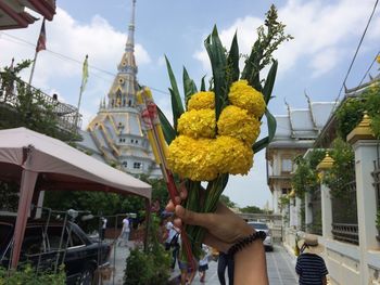 Cropped hand of person holding religious offerings against built structure and sky