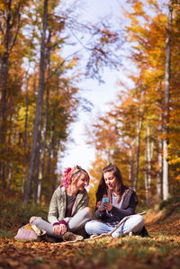 Friends talking while sitting on field against trees in forest during autumn