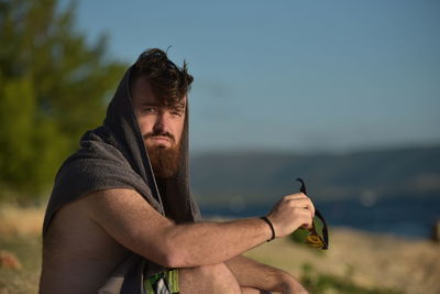 Portrait of bearded man sitting at beach against sky