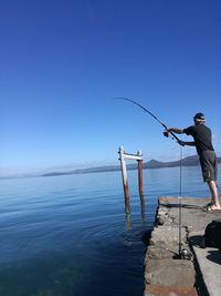 Man fishing by river against sky